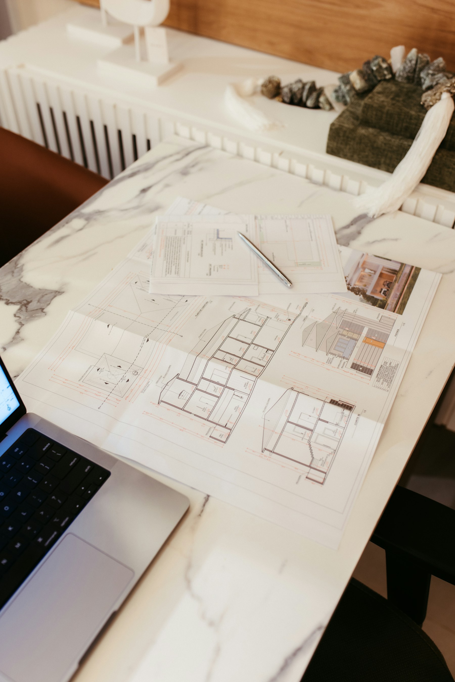 Architectural plans spread across a desk beside a laptop
